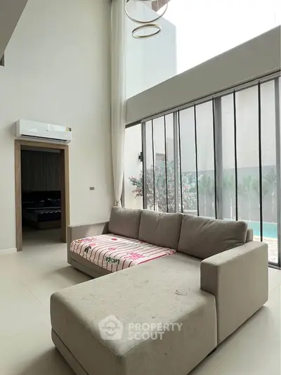 Spacious living room with large windows and modern sofa overlooking a pool area.