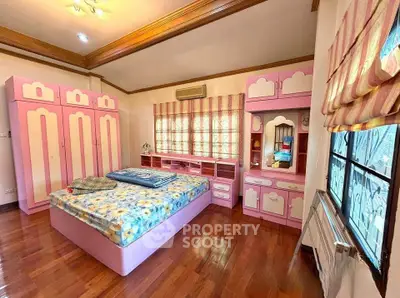 Charming bedroom with pink furniture and wooden flooring, featuring ample storage and natural light.