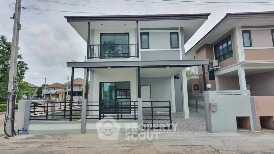 Modern two-story house with balcony and gated driveway in suburban neighborhood.