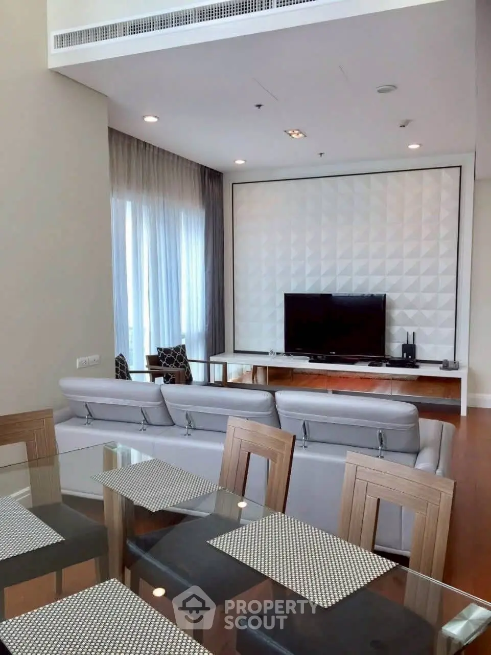 Modern living room with stylish decor and large TV, featuring elegant dining area and natural light.