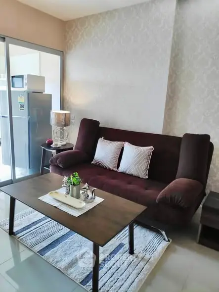 Modern living room with stylish sofa and coffee table, adjacent to a kitchen area with a refrigerator.