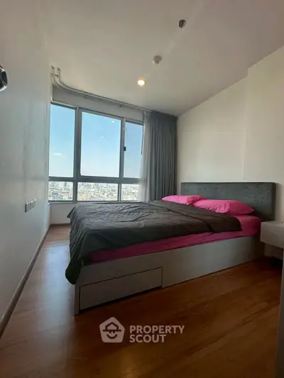 Modern bedroom with large window offering stunning city view and cozy decor.