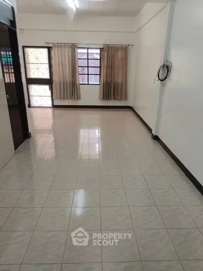 Spacious empty room with tiled flooring and large windows for natural light.