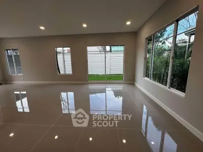 Spacious modern living room with large windows and glossy tiled floors, offering abundant natural light and garden view.
