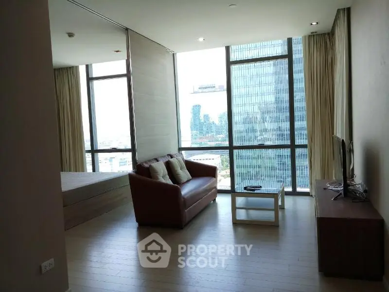 Modern living room with city view, featuring a cozy sofa and large windows in a high-rise apartment.
