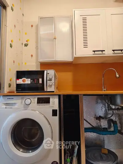 Compact kitchen with washing machine and microwave, ideal for small apartments.