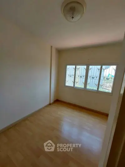 Bright empty room with wooden flooring and large window, perfect for customization.