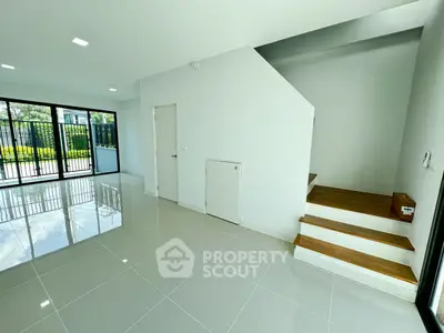 Spacious modern living room with glossy tiled floors and staircase, abundant natural light.