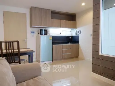 Modern compact kitchen with sleek cabinetry and cozy living area in open layout apartment.