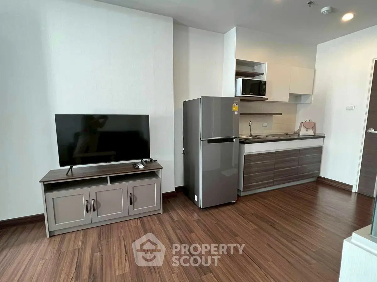 Modern apartment interior with sleek kitchen and cozy living area featuring a flat-screen TV and wooden flooring.