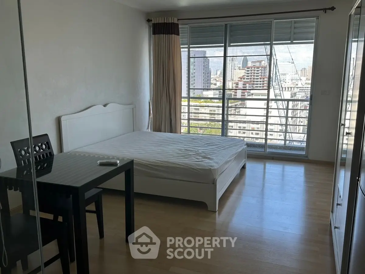 Spacious bedroom with city view and modern furnishings in high-rise apartment.