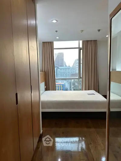 Cozy bedroom with city view, wooden flooring, and ample natural light in modern apartment.