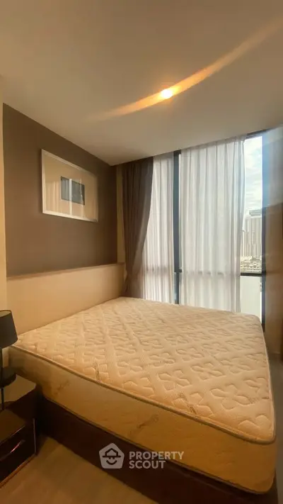 Spacious bedroom with large window and modern decor in urban apartment.