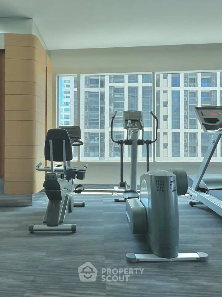 Modern gym with exercise equipment and city view in luxury building.