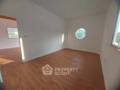 Spacious empty room with unique round window and wooden flooring