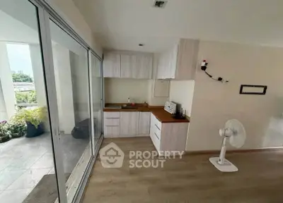 Modern kitchen with open layout and sliding glass doors to balcony, featuring sleek cabinetry and wooden flooring.