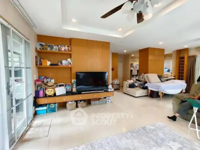 Spacious living room with modern decor and ample natural light, featuring a large TV and stylish shelving.