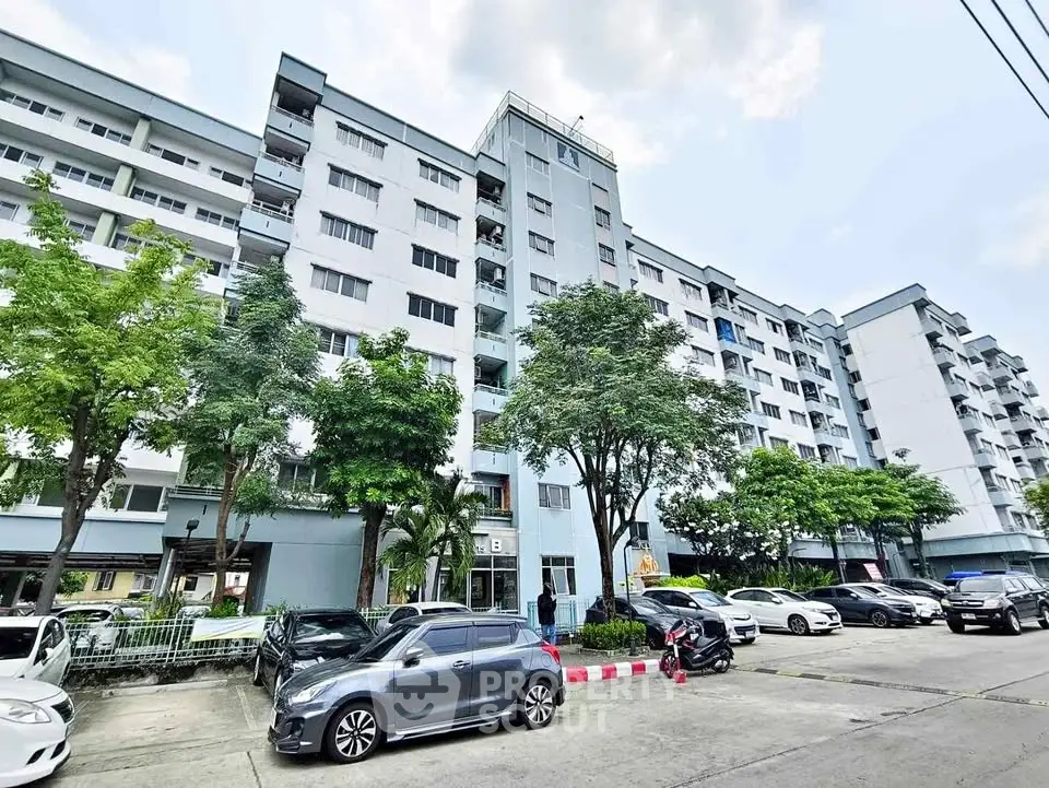 Modern multi-story residential building with parking and lush greenery.