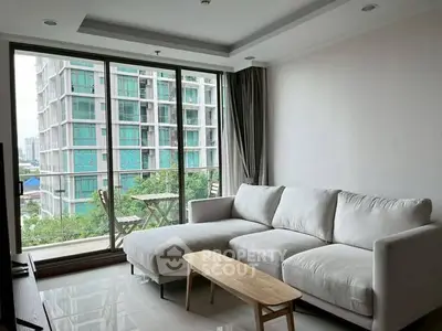 Modern living room with large windows and city view, featuring a cozy white sofa and sleek wooden table.