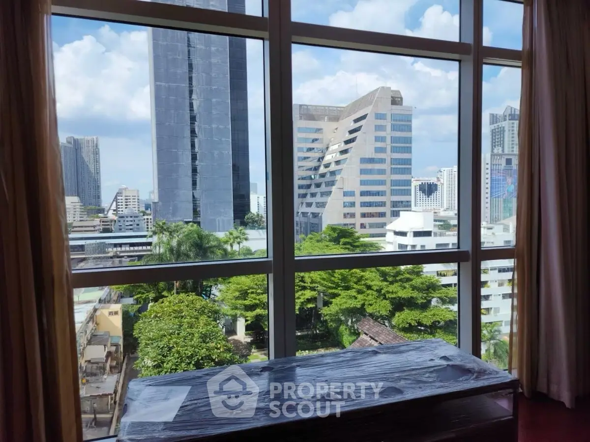 Stunning cityscape view from high-rise apartment window with lush greenery and modern skyscrapers.