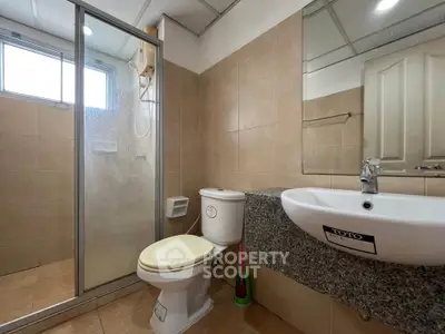 Modern bathroom with shower, toilet, and sink in a tiled setting.