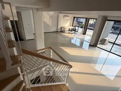 Spacious modern living room with large windows and sleek staircase, perfect for natural light lovers.