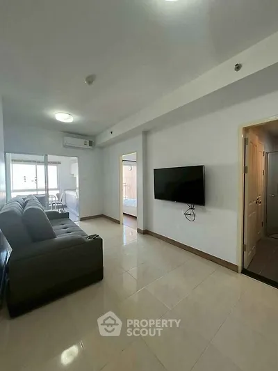 Spacious living room with modern sofa and wall-mounted TV, leading to a bright balcony.
