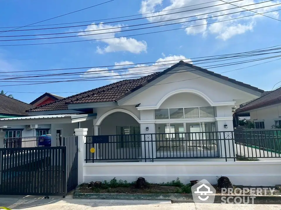 Charming single-story home with a classic tiled roof and large windows, nestled behind a secure fence in a serene neighborhood.