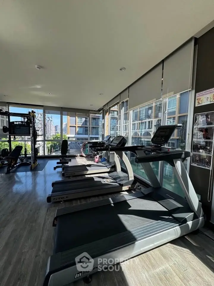 Modern gym with treadmills and weight equipment in a bright, spacious room with large windows.