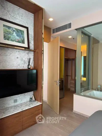 Modern bedroom with built-in TV, marble accents, and ensuite bathroom featuring a bathtub.