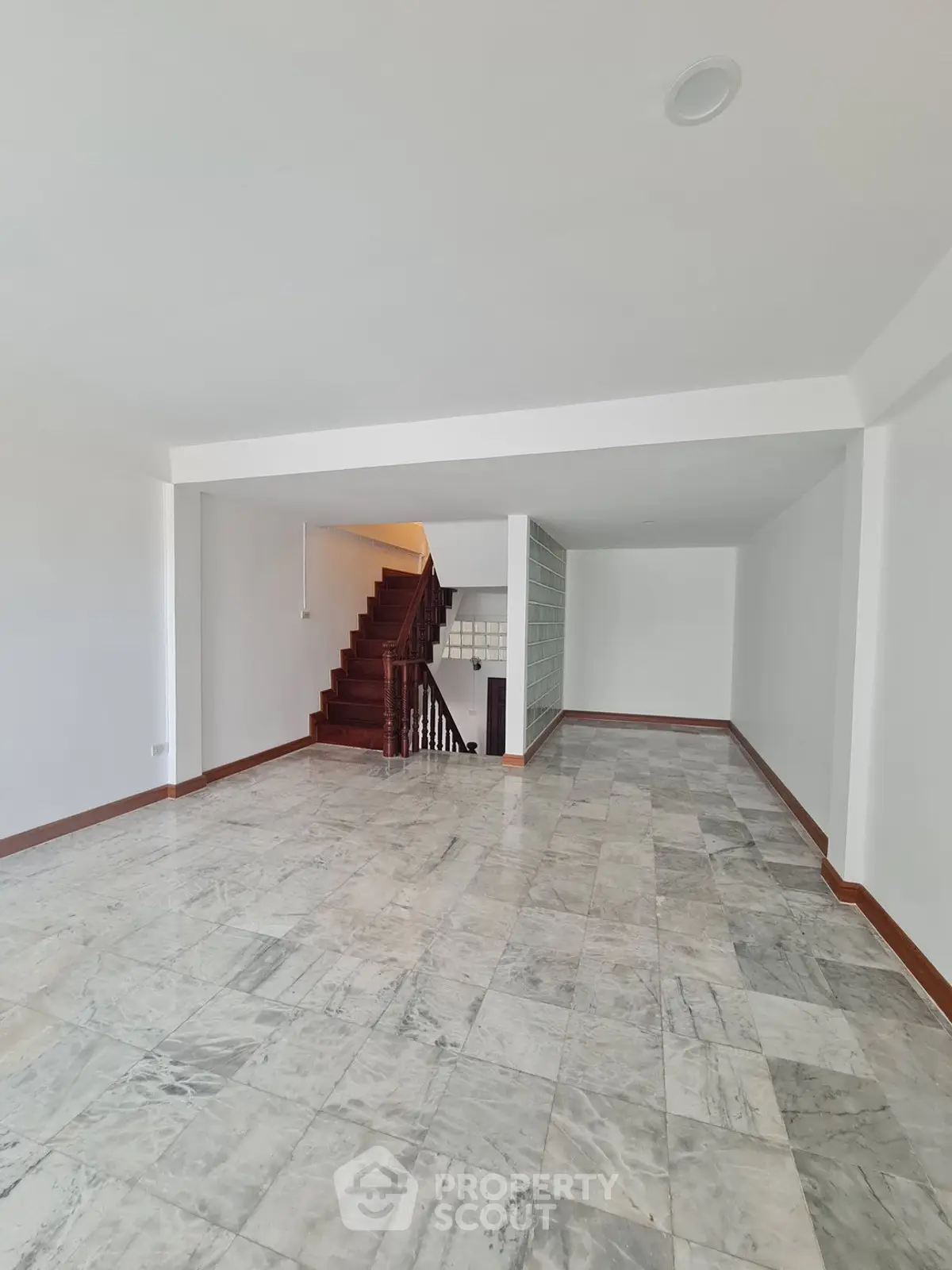 Spacious open-plan living area with elegant marble flooring and wooden staircase, perfect for modern living.