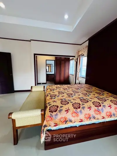 Spacious bedroom with elegant wooden furniture and floral bedspread, featuring ample natural light and cozy ambiance.