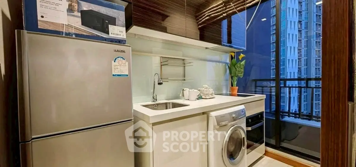 Modern kitchen with stainless steel fridge and washing machine, city view balcony.