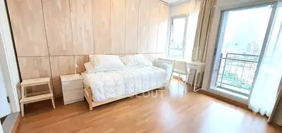 Spacious bedroom with wooden flooring and balcony view in modern apartment.