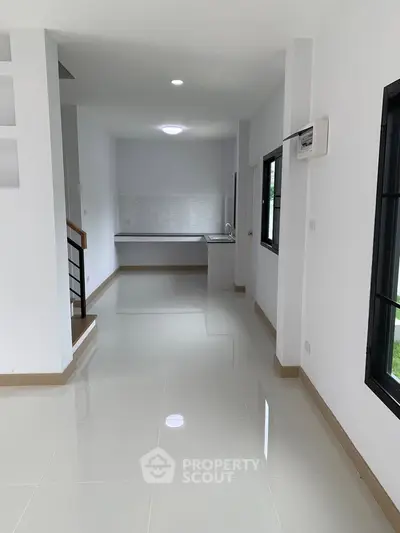 Spacious modern interior with sleek white walls and glossy floors, featuring a minimalist kitchen area.