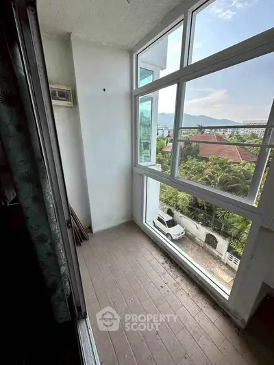 Bright balcony with large windows offering scenic views of lush greenery and distant mountains.