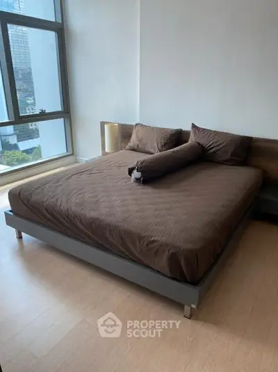 Spacious bedroom with large window offering city views, featuring a modern bed and sleek wooden flooring.