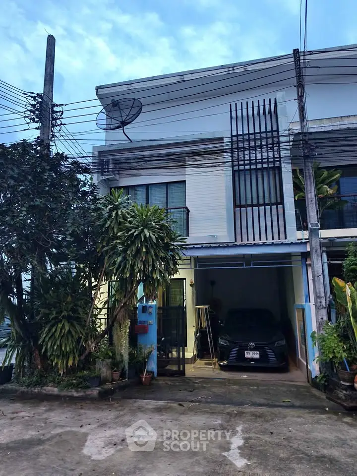 Charming two-story townhouse with carport and lush greenery in a serene neighborhood.