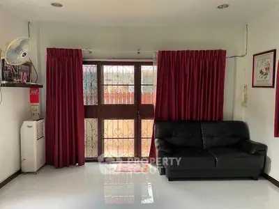 Cozy living room with red curtains, black leather sofa, and polished white floor tiles.