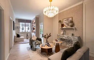 Elegant living room with modern decor and stylish chandelier, featuring a cozy seating area and large window.