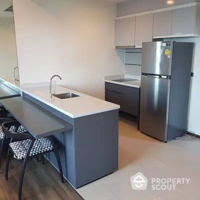 Modern kitchen with sleek cabinetry, stainless steel refrigerator, and a spacious island with a sink, ideal for culinary enthusiasts.