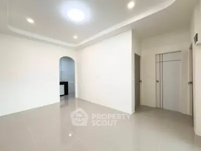 Spacious modern living room with sleek tile flooring and recessed lighting, leading to a stylish kitchen.