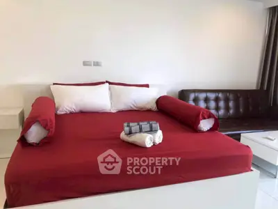 Spacious bedroom with modern red bedding and stylish sofa, perfect for comfort and relaxation.