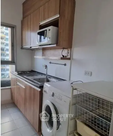 Modern kitchen with wooden cabinets, washing machine, and microwave in a compact layout.
