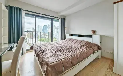 Modern bedroom with city view, featuring a cozy bed and large window for natural light.