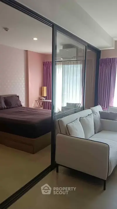 Modern apartment with glass partition separating bedroom and living area, featuring stylish decor.
