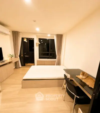 Modern bedroom with cozy decor and a cat on the desk, featuring a large window and stylish furnishings.