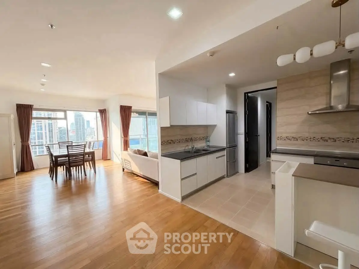 Spacious open-plan living and kitchen area with city view, featuring modern appliances and elegant wooden flooring.