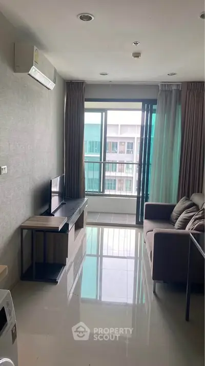 Modern living room with large window and balcony view, featuring sleek furniture and air conditioning.