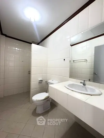 Spacious white-tiled bathroom with modern fixtures and ample lighting